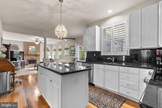 kitchen featuring a sink, a fireplace, ceiling fan with notable chandelier, stainless steel dishwasher, and a kitchen island