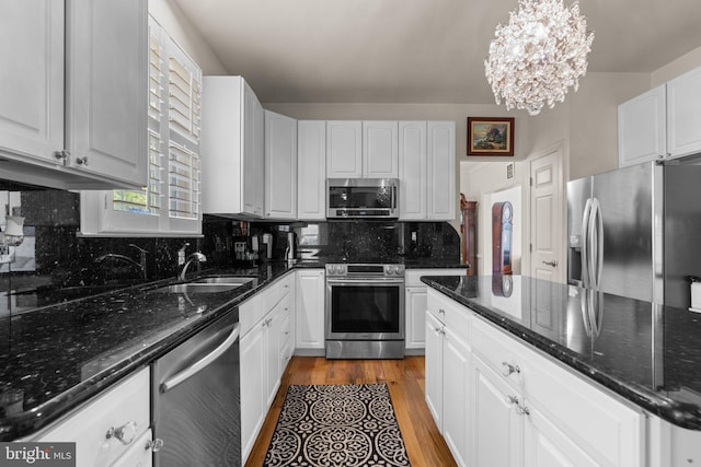 kitchen with white cabinets, dark wood-style flooring, a sink, stainless steel appliances, and decorative backsplash