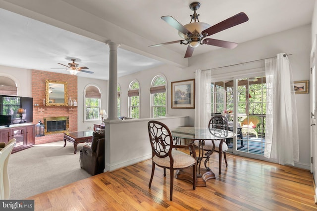 dining room featuring wood-type flooring, beam ceiling, a fireplace, ornate columns, and a ceiling fan