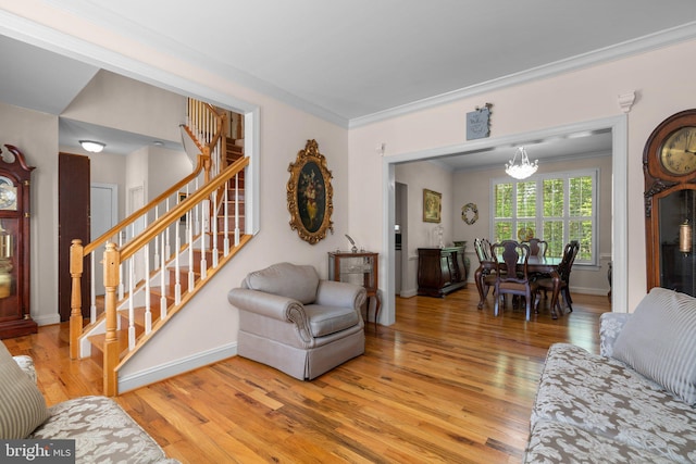 living room featuring crown molding, stairway, baseboards, an inviting chandelier, and light wood-style flooring