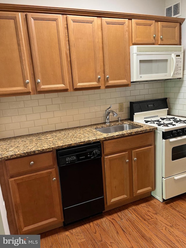 kitchen featuring visible vents, stone counters, white appliances, a sink, and light wood-style flooring
