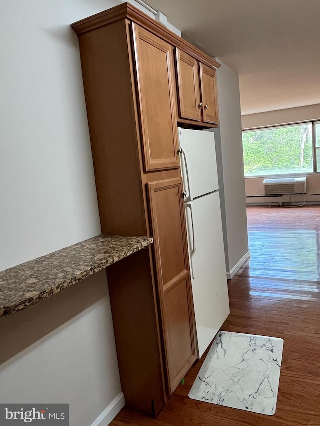 kitchen with baseboards, freestanding refrigerator, dark wood-style flooring, and dark stone countertops