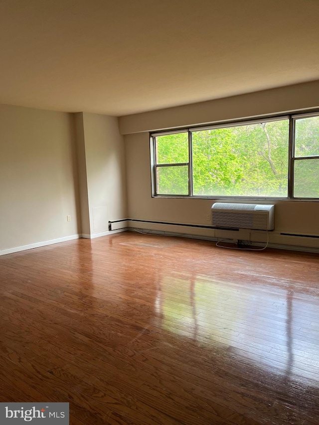 spare room featuring baseboards, a baseboard heating unit, and wood finished floors