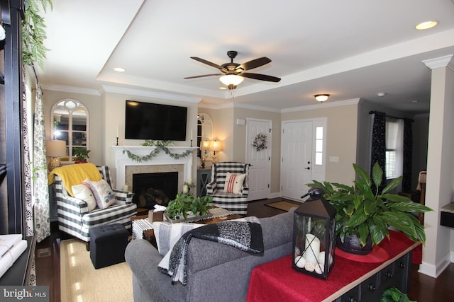 living room featuring a ceiling fan, a fireplace, dark wood finished floors, baseboards, and a tray ceiling