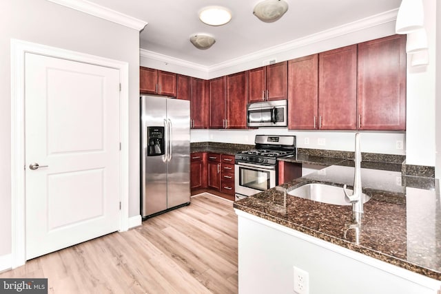 kitchen with ornamental molding, reddish brown cabinets, dark stone counters, a sink, and stainless steel appliances