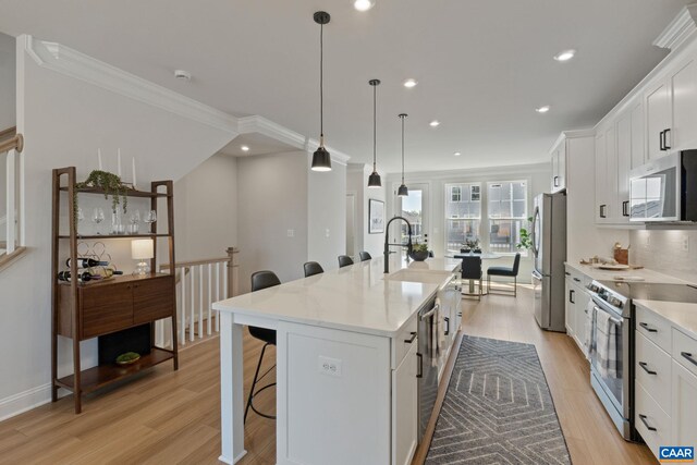 kitchen featuring a breakfast bar area, a center island with sink, white cabinets, light wood-style flooring, and stainless steel appliances