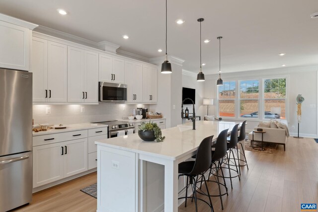 kitchen with light wood-style floors, an island with sink, stainless steel appliances, backsplash, and ornamental molding