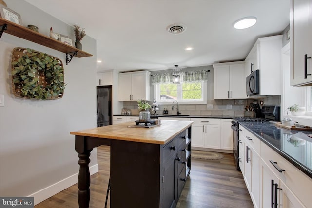 kitchen featuring a sink, white cabinets, black appliances, a breakfast bar, and butcher block countertops