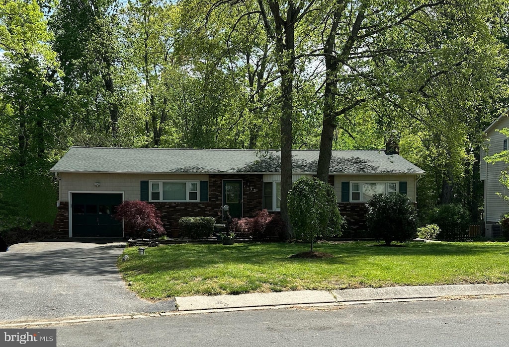 ranch-style house with a chimney, a garage, brick siding, aphalt driveway, and a front lawn