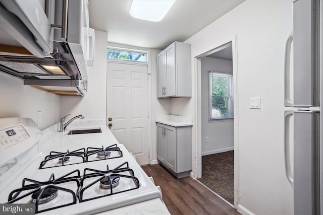 kitchen with light stone countertops, a sink, white appliances, dark wood finished floors, and gray cabinets