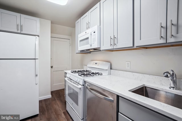 kitchen featuring light stone countertops, dark wood finished floors, a sink, baseboards, and white appliances