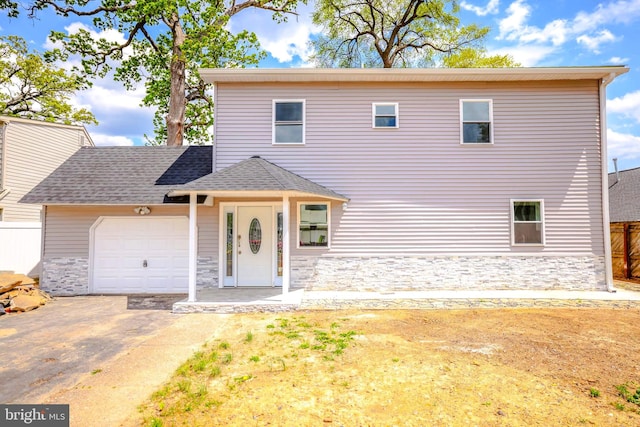 traditional home with roof with shingles, fence, concrete driveway, an attached garage, and stone siding