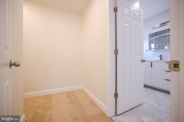 hallway featuring baseboards, light carpet, and a sink