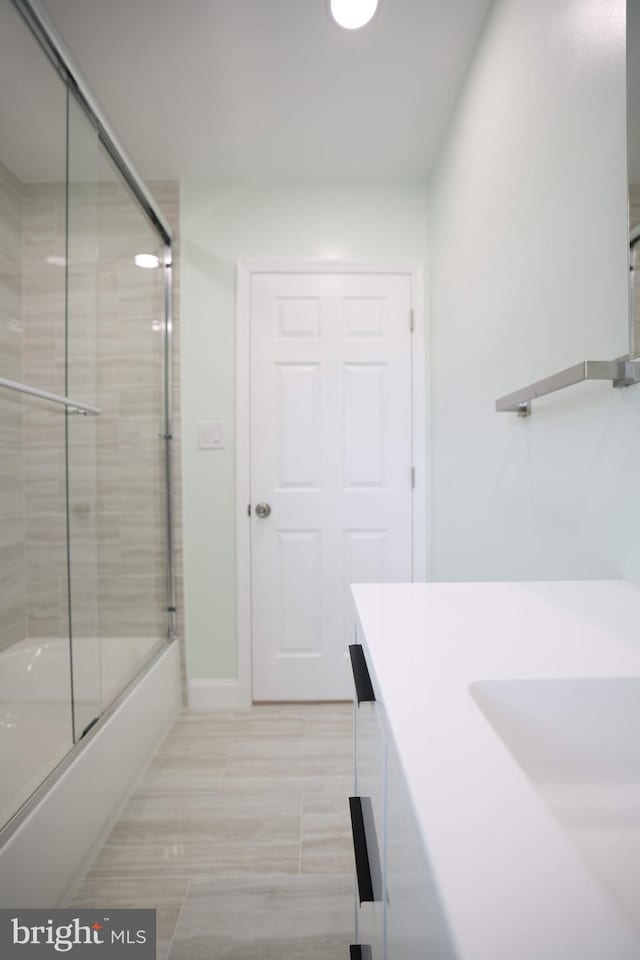 bathroom featuring vanity, baseboards, and combined bath / shower with glass door