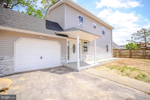 view of front of house with fence, a shingled roof, stone siding, a garage, and driveway