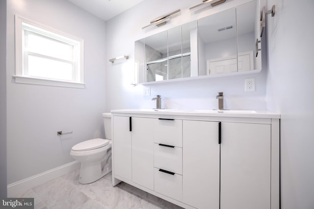 bathroom with double vanity, marble finish floor, toilet, baseboards, and a sink