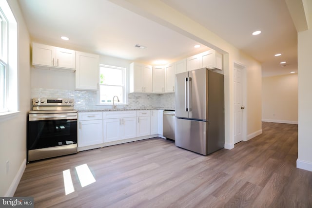 kitchen with decorative backsplash, appliances with stainless steel finishes, a sink, baseboards, and white cabinetry