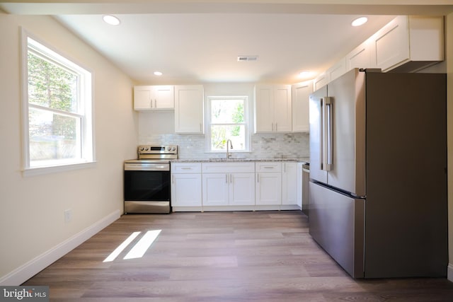 kitchen with decorative backsplash, visible vents, a sink, white cabinets, and stainless steel appliances