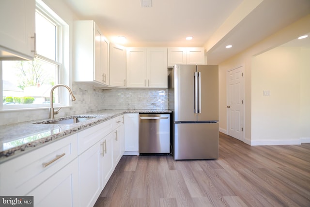 kitchen with a sink, white cabinets, backsplash, and stainless steel appliances