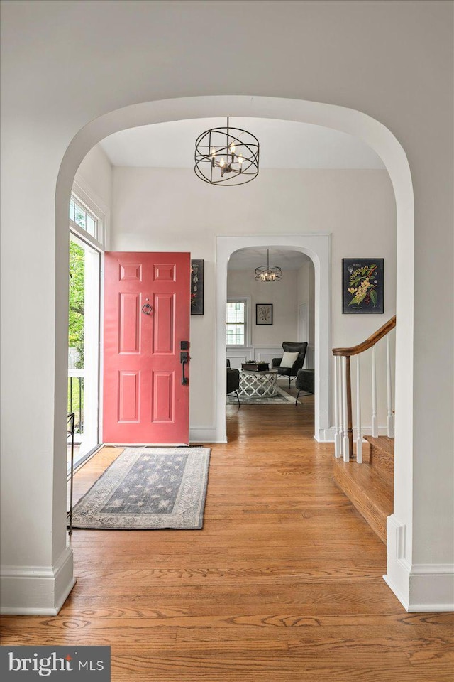 entrance foyer with arched walkways, wood finished floors, baseboards, a chandelier, and stairs