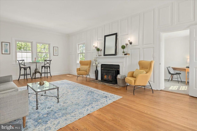 living room with a fireplace with flush hearth, ornamental molding, a decorative wall, and light wood-type flooring