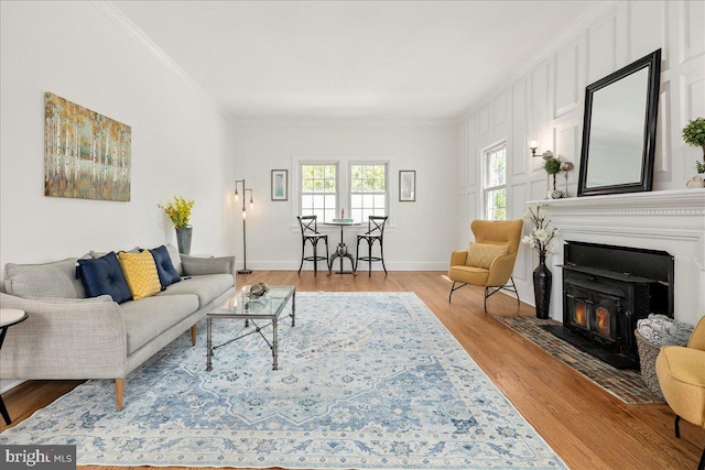 living room featuring baseboards, a fireplace with flush hearth, ornamental molding, and light wood finished floors