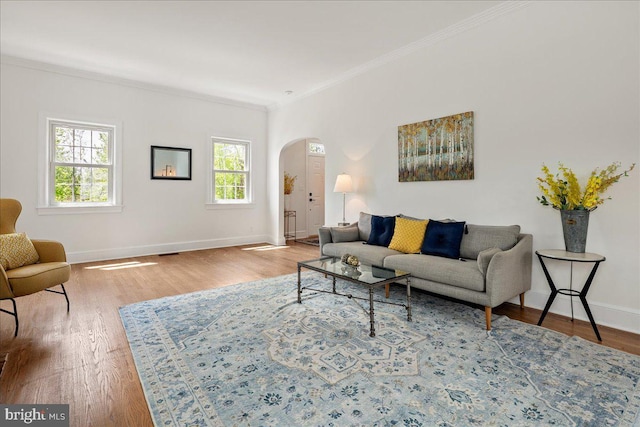 living room featuring arched walkways, ornamental molding, baseboards, and wood finished floors