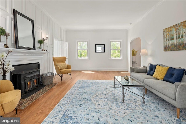 living area featuring crown molding, arched walkways, light wood finished floors, and baseboards