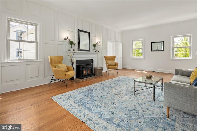 living area featuring crown molding, baseboards, a fireplace with flush hearth, and light wood-type flooring