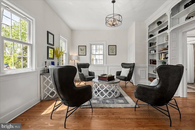 sitting room featuring a wainscoted wall, a notable chandelier, a healthy amount of sunlight, and wood finished floors