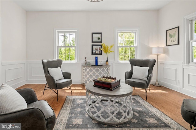 living area with a decorative wall, wainscoting, and wood finished floors