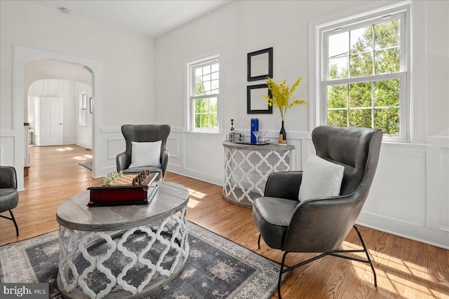 living area with arched walkways, a wainscoted wall, a decorative wall, and wood finished floors