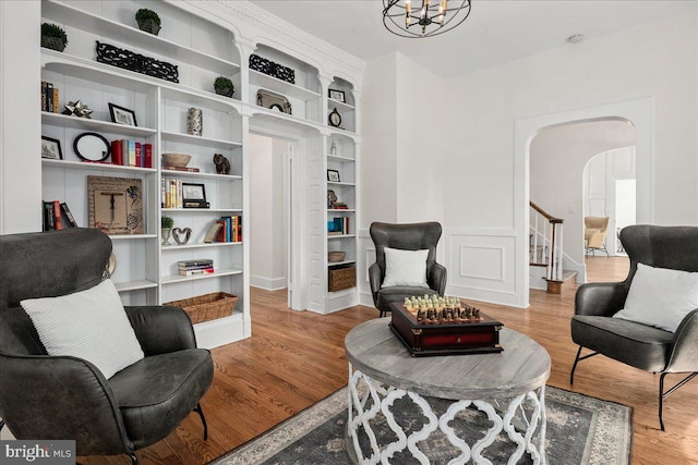 living area with an inviting chandelier, arched walkways, wood finished floors, and stairway