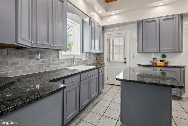 kitchen with light tile patterned floors, gray cabinets, decorative backsplash, and a sink
