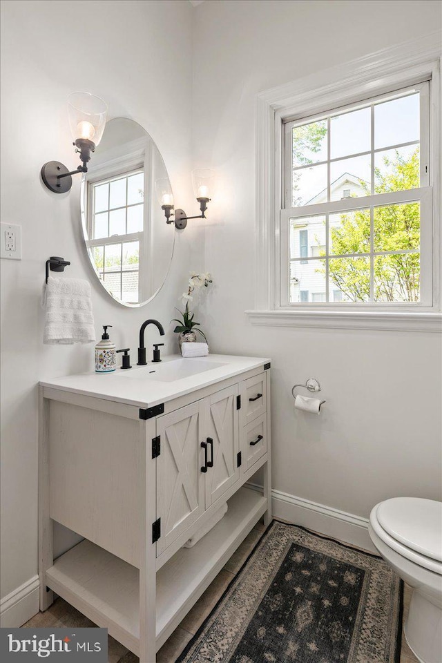 half bathroom featuring baseboards, plenty of natural light, toilet, and vanity