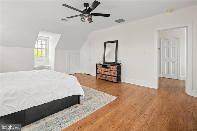bedroom with baseboards, lofted ceiling, wood finished floors, and visible vents