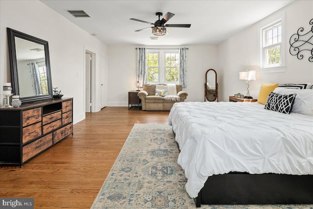 bedroom featuring baseboards, visible vents, multiple windows, and wood finished floors