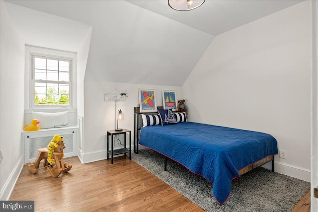 bedroom featuring baseboards, radiator heating unit, wood finished floors, and lofted ceiling