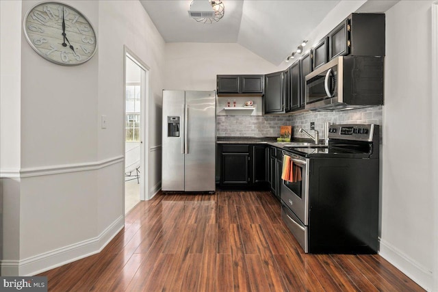 kitchen with lofted ceiling, dark countertops, dark wood finished floors, appliances with stainless steel finishes, and backsplash