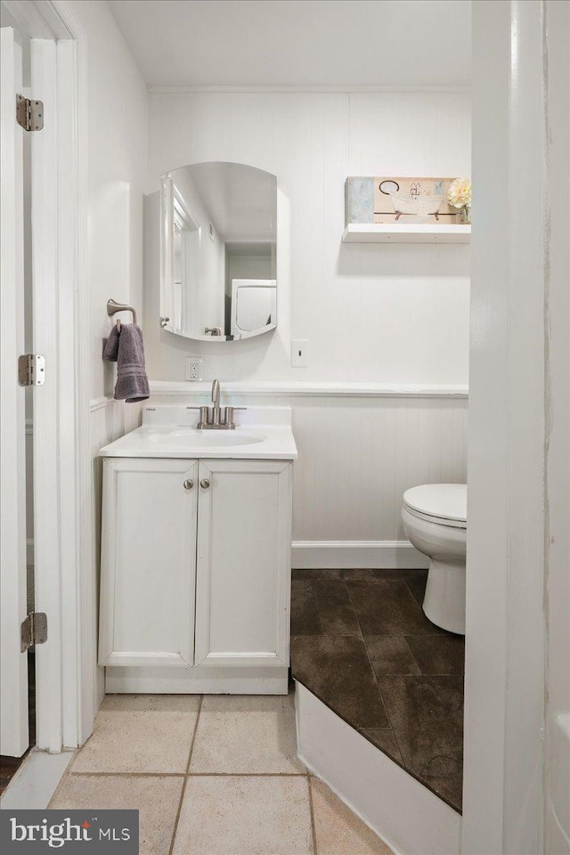 half bathroom featuring toilet, wainscoting, and vanity