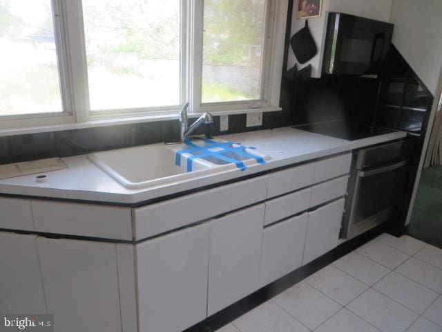 kitchen featuring a sink, white cabinetry, black appliances, and a wealth of natural light