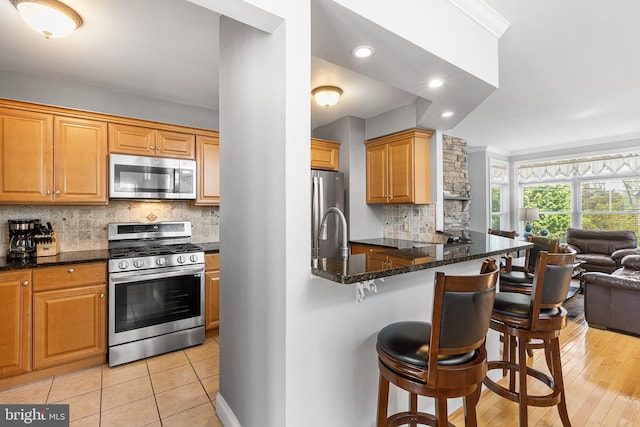 kitchen with appliances with stainless steel finishes, open floor plan, a breakfast bar area, dark stone countertops, and tasteful backsplash