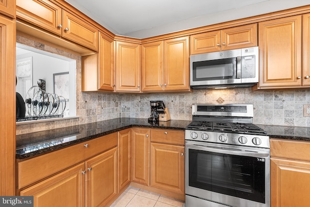 kitchen featuring appliances with stainless steel finishes, dark stone counters, light tile patterned floors, and backsplash