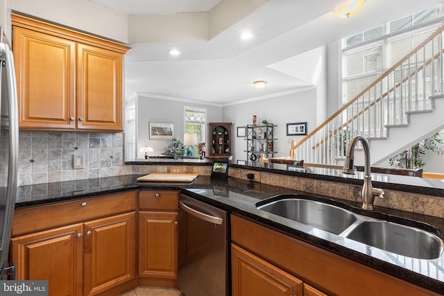 kitchen featuring appliances with stainless steel finishes, a sink, dark stone countertops, crown molding, and brown cabinets