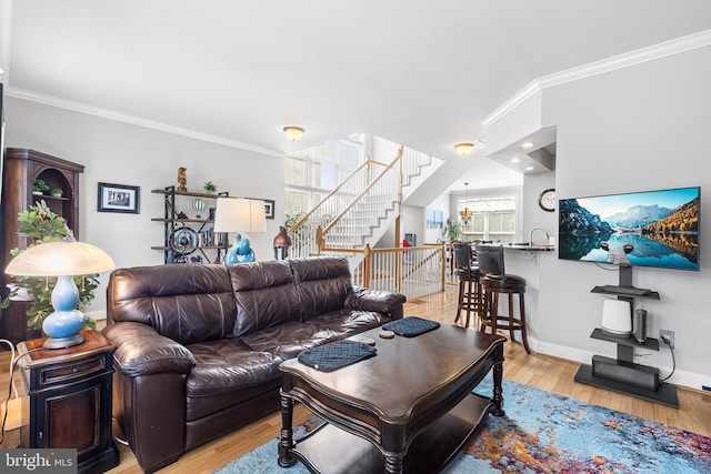 living area with crown molding, stairs, light wood-type flooring, and baseboards