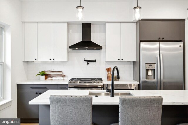 kitchen with wall chimney range hood, appliances with stainless steel finishes, tasteful backsplash, and pendant lighting