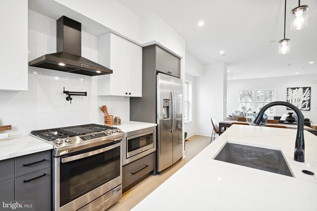 kitchen with backsplash, appliances with stainless steel finishes, hanging light fixtures, a sink, and wall chimney exhaust hood