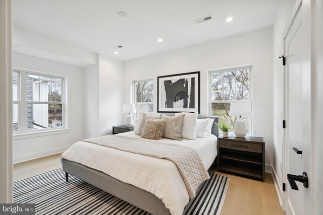 bedroom featuring baseboards, visible vents, multiple windows, and light wood finished floors