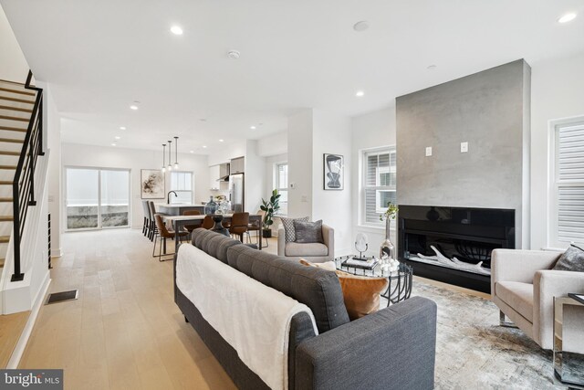 living area featuring light wood finished floors, a fireplace, recessed lighting, visible vents, and stairway