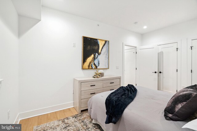 bedroom featuring light wood-style floors, baseboards, two closets, and recessed lighting